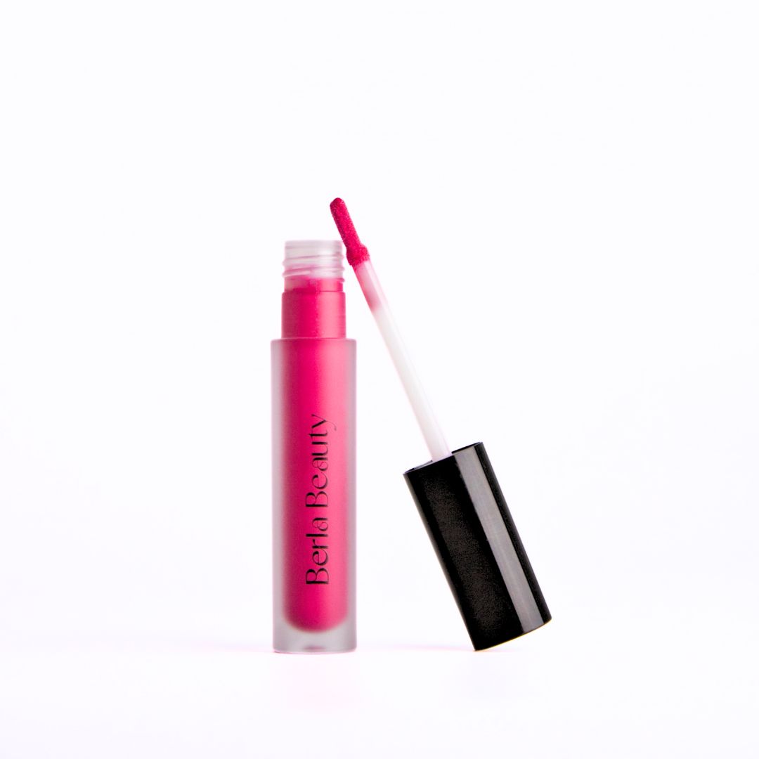 A bright pink, vegan, and paraben-free liquid lip gloss in a frosted bottle labeled &quot;Berla Beauty&quot; with the cap off, revealing a doe-foot applicator. The black cap is placed slightly tilted next to the bottle against a plain white background, promising long-lasting shine. This product is the Brilliance Lip Gloss - Cruelty-free &amp; Vegan.