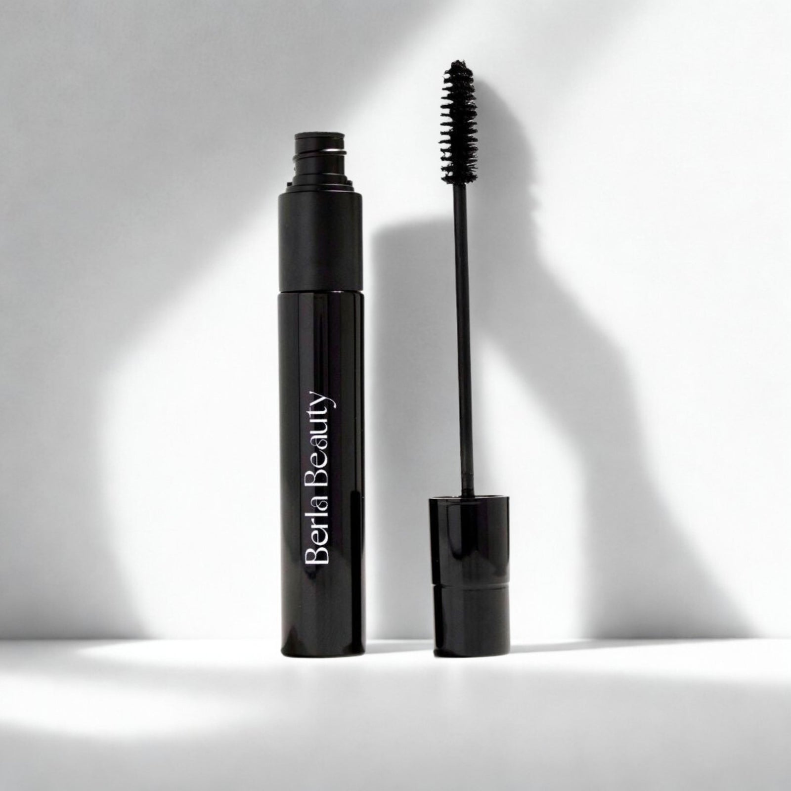 Three black mascara tubes from Berla Beauty are shown, with one open to reveal its mascara wand. The design is sleek and minimalist, featuring the brand name "Berla Beauty" in white letters on the tube. Notably, this "Vegan Dual Lash Long Lasting Mascara - Bold and Beautiful Lashes" boasts a lightweight formula that is both vegan and cruelty-free.