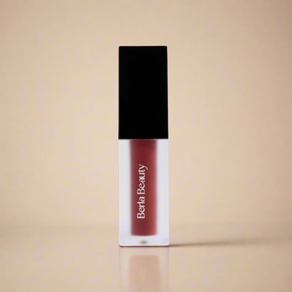 A tube of vegan-friendly Vegan Matte Lip Stain - Long Lasting, Moisturizing, and Pigment Rich from Berla Beauty stands upright against a beige background. The lipstick has a clear base displaying the product color and a black rectangular cap. The brand name is printed vertically in white on the front of the tube.