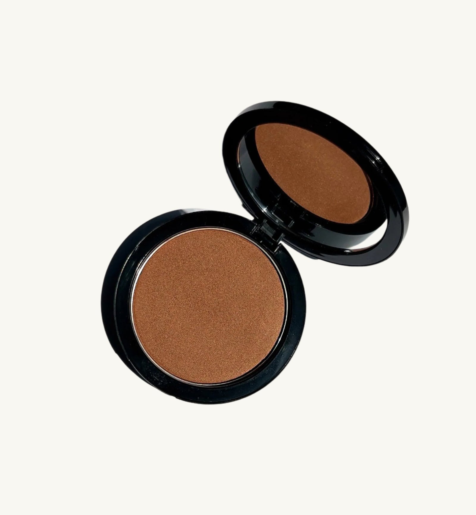 A round, open compact with a mirror in the lid, featuring Berla Beauty's Vegan Talc-Free Bronzer Powder. This vegan bronzer offers a single shade of natural tan pressed powder, ideal for makeup application. Encased in a sleek black housing, the mirror perfectly reflects the powder within.