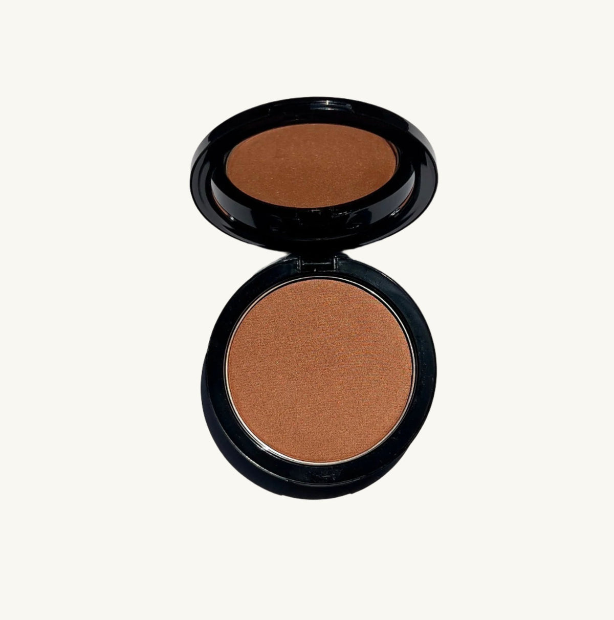 A black compact case with the lid open reveals Berla Beauty&#39;s Vegan Talc-Free Bronzer Powder in a natural tan shade, expertly balanced for a flawless finish. The underside of the lid features a small mirror, making it perfect for on-the-go application. The vegan bronzer compact is set against a plain white background.