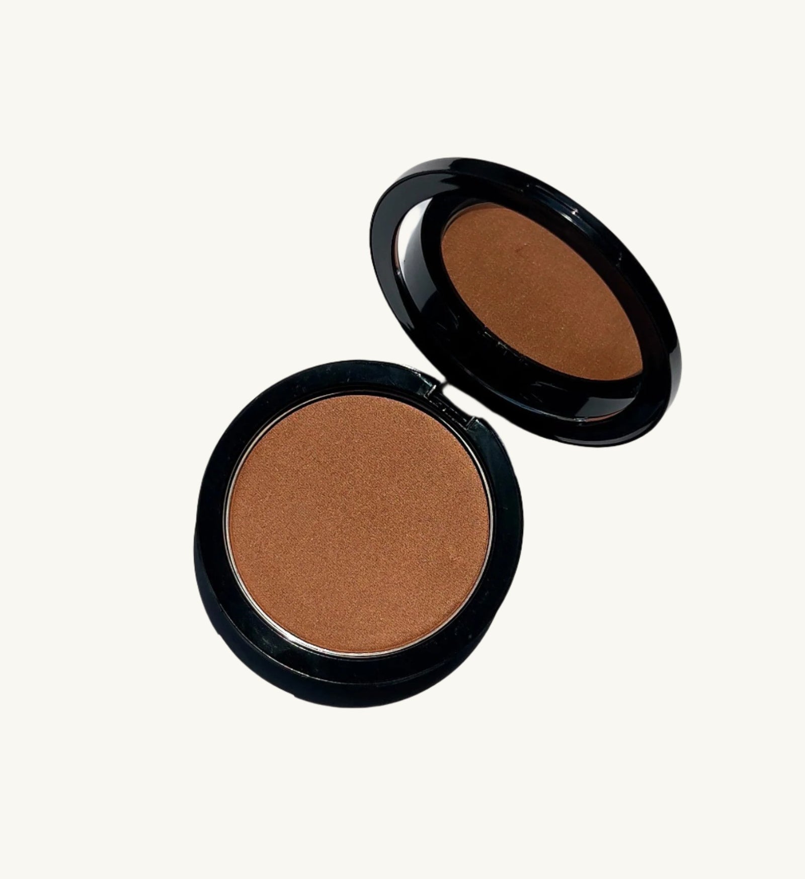 A round, open compact with a mirror in the lid, featuring Berla Beauty's Vegan Talc-Free Bronzer Powder. This vegan bronzer offers a single shade of natural tan pressed powder, ideal for makeup application. Encased in a sleek black housing, the mirror perfectly reflects the powder within.