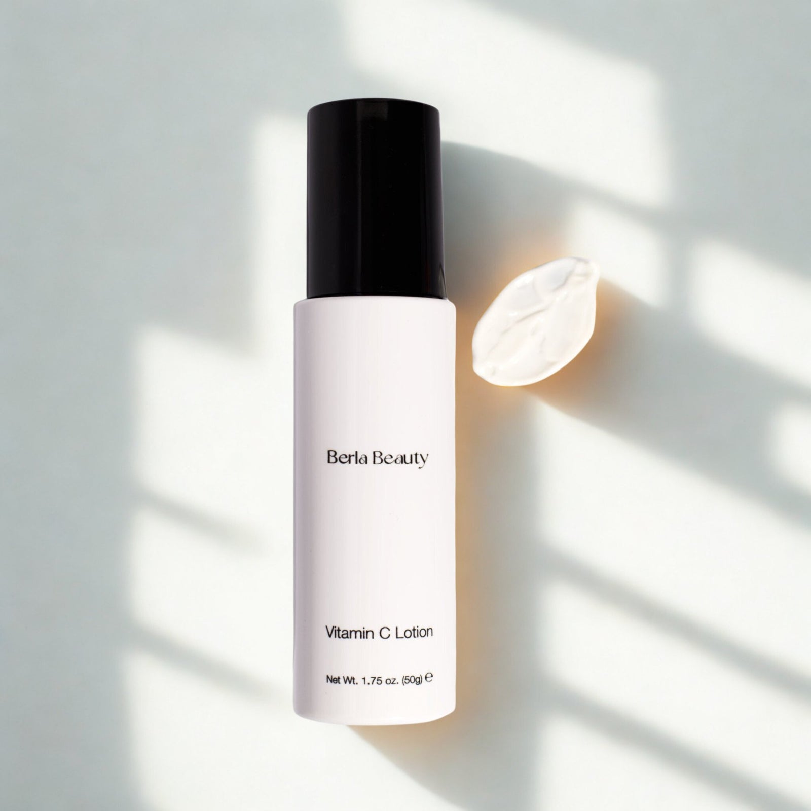 A sleek white bottle with a black cap, labeled "Berla Beauty" and "Vitamin C Lotion," boasts a clean, minimalist design against a plain beige background. This 1.75 oz (50 grams) product promises to brighten the skin while providing deep hydration.